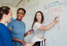 A photo of a teacher and two high school students at a whiteboard and solving algebra problems.