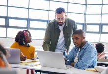 Teacher talking to two students as they complete a daily routine on computers