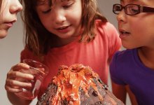 A photo of three upper elementary students observing a model volcano after pouring liquid into it.