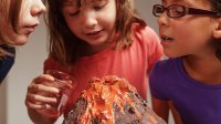 A photo of three upper elementary students observing a model volcano after pouring liquid into it.