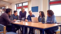 A photo of teachers and paraprofessionals sitting at a table in a school library and having a discussion.