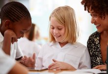 A photo of a teacher assisting two elementary students with a group assignment.