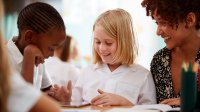 A photo of a teacher assisting two elementary students with a group assignment.