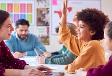 A photo of two teachers working with two groups of elementary students in a classroom.