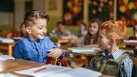 A photo focusing on two elementary students talking through group work at their desks.