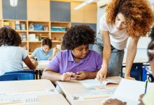 A photo of a teacher helping a student at their desk during class work time.