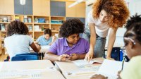 A photo of a teacher helping a student at their desk during class work time.