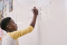 A photo of an elementary student solving square multiplication problems on the class whiteboard.