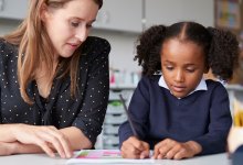 A photo of an elementary student being guided through an assignment by their teacher.