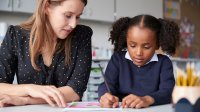 A photo of an elementary student being guided through an assignment by their teacher.