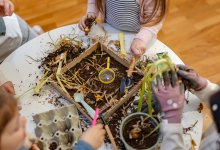 A photo of young elementary students interacting with dirt and compost materials laid out on a table.