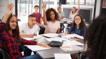 A photo of students sitting in a classroom and raising their hands to participate in a student-led discussion.