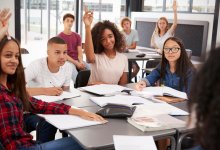 A photo of students sitting in a classroom and raising their hands to participate in a student-led discussion.
