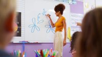 A photo of an elementary teacher drawing flower petals to demonstrate fractions on a whiteboard.