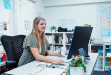 A photo of a teacher at her desk working on a desktop computer.