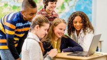 A photo of middle school students in a social studies classroom doing group work on a computer.