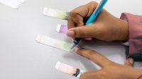 A photo of a student taking notes of four ink chromatography results.