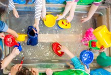 A overhead shot of preschoolers playing with different tools and toys at a water table.