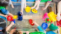A overhead shot of preschoolers playing with different tools and toys at a water table.