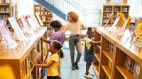 A photo of a teacher supervising as elementary students organize books in the library.