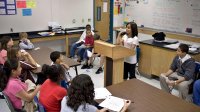 A photo of a middle school classroom debate. One student is speaking at a podium in front the rest of her classmates.