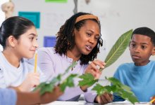A photo of a teacher and her elementary students holding up leaves as they document them in a journal.