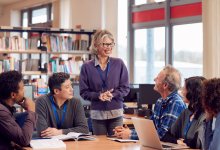 A photo of a group of teachers having a meeting with an administrator in a school library.