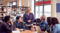 A photo of a group of teachers having a meeting with an administrator in a school library.