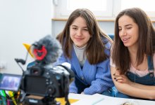 A photo of a middle school student recording a school project with her sister at their home.