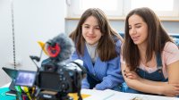A photo of a middle school student recording a school project with her sister at their home.