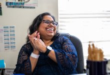 A photo of a teacher sitting at her desk and laughing at what someone out of the frame said.