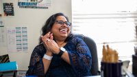 A photo of a teacher sitting at her desk and laughing at what someone out of the frame said.