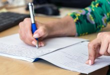 A photo focused on an administrator's hands as they write in a journal at their desk.