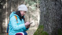 A photo of an elementary student writing on a notepad while observing a tree trunk.