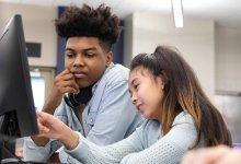 A photo of a high school student guiding an elementary student through a STEM lesson on a computer.