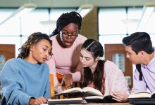 A photo of four students working on a group project in a library.
