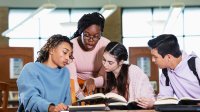 A photo of four students working on a group project in a library.