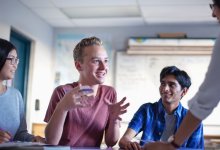 A photo of a teacher talking to a small group of engaged middle school students.
