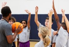 A photo of middle school students in PE class enthusiastically raising their hands to their teacher.