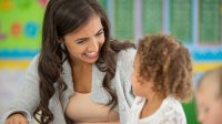A photo of a preschool teacher calmly talking to one of their students.