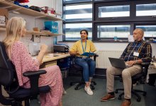A photo of a small group of teachers having a meeting inside of an office.