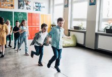 A photo of elementary students walking in a straight line over the long crack in between the tiles on the floor.