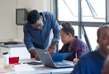 A photo of a high school teacher giving one of their students feedback during class.