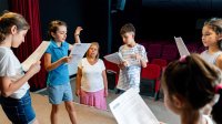 A photo of elementary students rehearsing a skit in their school auditorium.