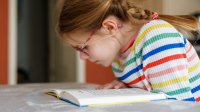 A photo of an elementary student reading a book in her home. empowering elementary readers