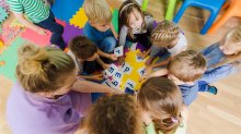 A photo of preschool students and their teacher circling around alphabet flashcards.