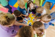 A photo of preschool students and their teacher circling around alphabet flashcards.