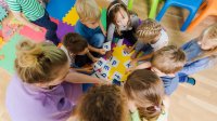 A photo of preschool students and their teacher circling around alphabet flashcards.