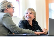 Two administrators having a discussion while referring to notes on a laptop