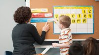 A photo of a teacher guiding one of her preschool students in an activity about the days of the week